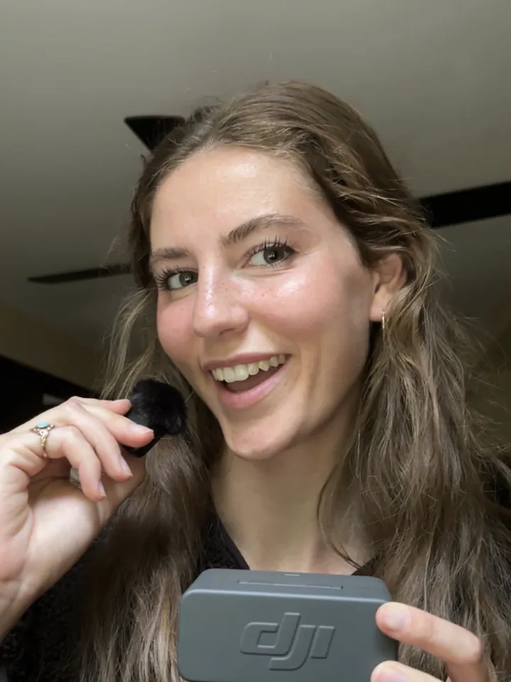 Allie smiling while holding a DJI wireless microphone and its windscreen
