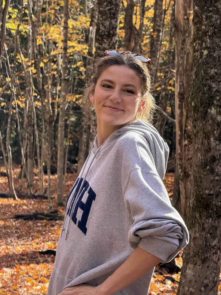 Allie in a grey hoodie smiling over her shoulder in an autumn forest